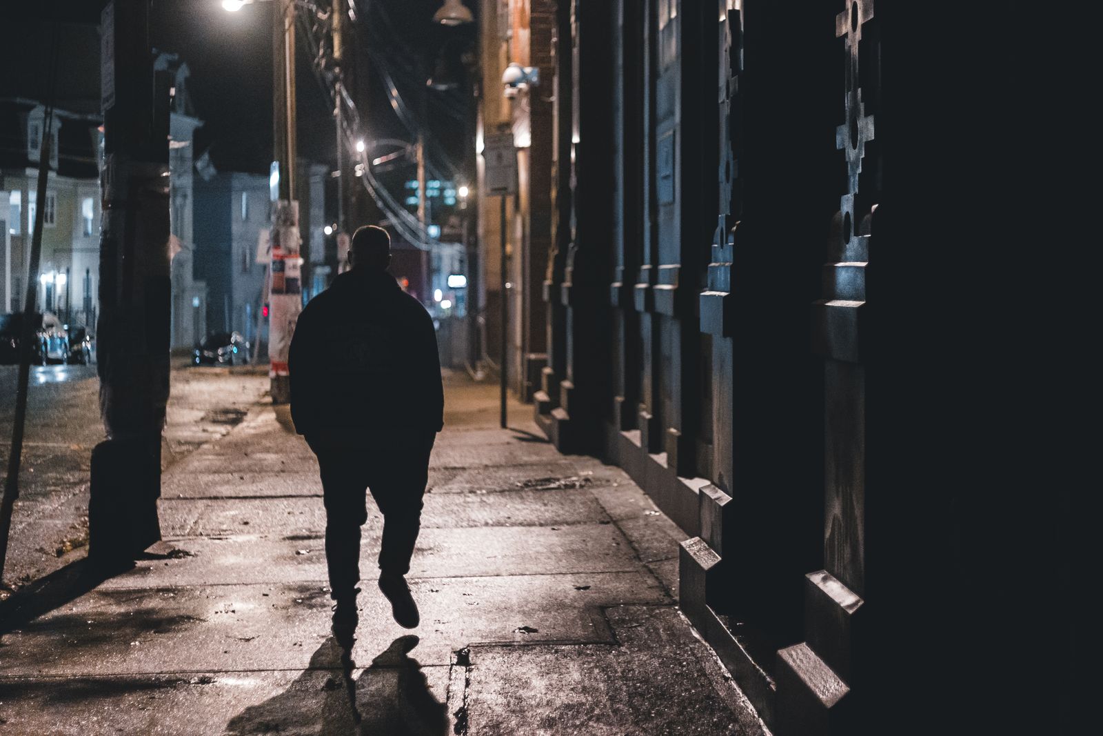 Silueta de un hombre que camina solo por una calle mojada de noche.