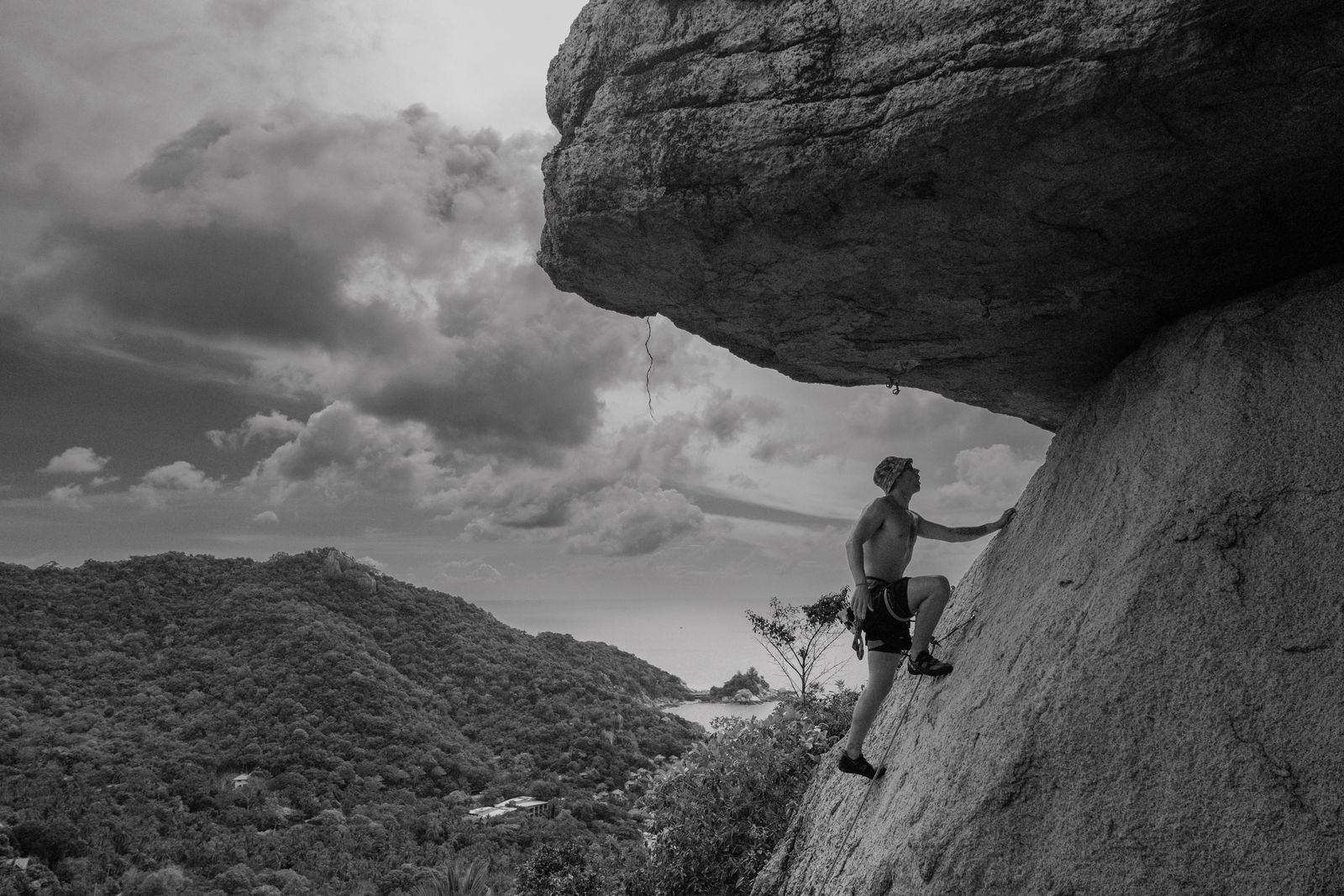 Un hombre escala una pared de roca bajo un cielo nublado.
